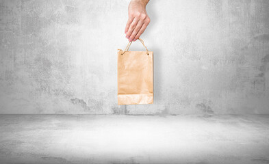 Paper bag in hand on a stone background. Concept of using ecological items. The man holds a brown bag with a gift, purchases in his hand. Giving gifts.