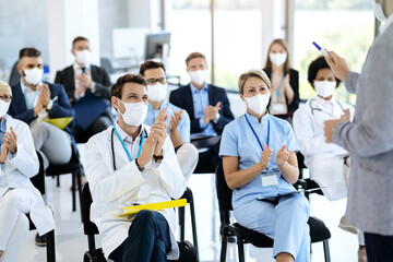 Healthcare workers and business people wearing face masks and applauding on a seminar.