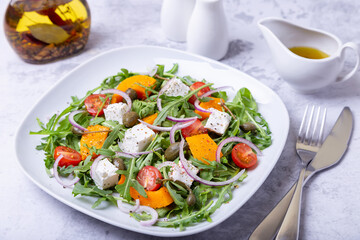 Warm salad with pumpkin, feta cheese, tomatoes, capers, arugula and red onion. Close-up.
