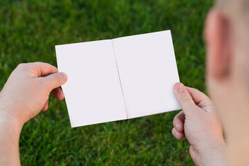 Layout of the cover of the magazine, catalog, book. a man reading a blank magazine, catalog, book sitting on a green lawn