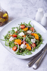 Warm salad with pumpkin, feta cheese, tomatoes, capers, arugula and red onion. Close-up.