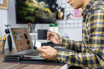 Asian man holding credit card and typing information on internet with laptop at home, online shopping concept.