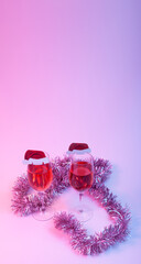 Christmas and new year holiday greeting card concept with two wine glasses with rose wine decorated with Santa hats on multicolored  background. Copy space.
