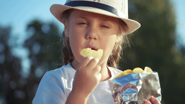 child eating chips close-up face. kid resting in the park eating chips. little girl resting on a picnic in the park eating potato chips. kid dream lifestyle concept