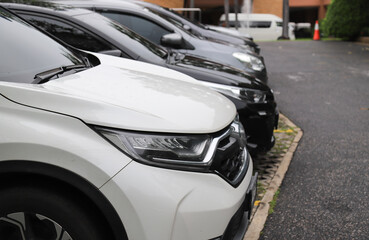 Closeup of front side of white car and other cars parking in parking area in rainy day.