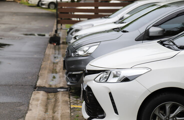 Closeup of front side of white car  with other cars parking in parking area in rainy day.