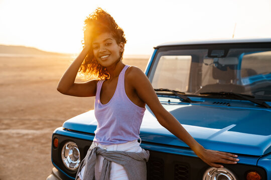 Image of cheerful african american woman smiling while travelling with car on desert