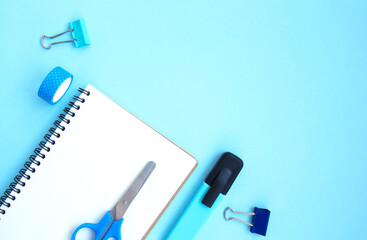 White open notebook with blue marker, clamps, scissors and scotch on a blue background with space for text. Getting ready for school. Creative workspace with stationery. Back to school. Flat lay