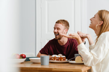 Photo of joyful beautiful couple talking while drinking tea with pie