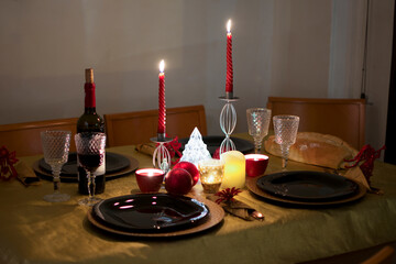Elegant and cozy table with a bottle of wine and candles that give an intimate light, all prepared for Christmas dinner. 