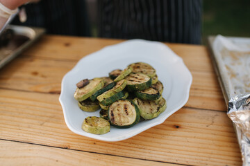Waiter in white gloves put grilled vegetables on plate outdoors