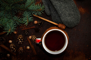 Obraz na płótnie Canvas Winter background with a branch of a Christmas tree. A cup of hot tea with lemon, dressed in a knitted warm winter scarf on a rusty metal background.