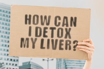 The phrase " How can I detox my liver? " on a banner in men's hand with blurred background. Health care. Organ. Body. Biology. Hospital. Recommendation