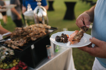 First person view of somebody hold plate and take some snack on plate. Outdoor party