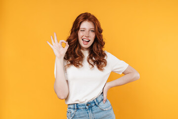 Image of ginger joyful girl winking and gesturing ok sign