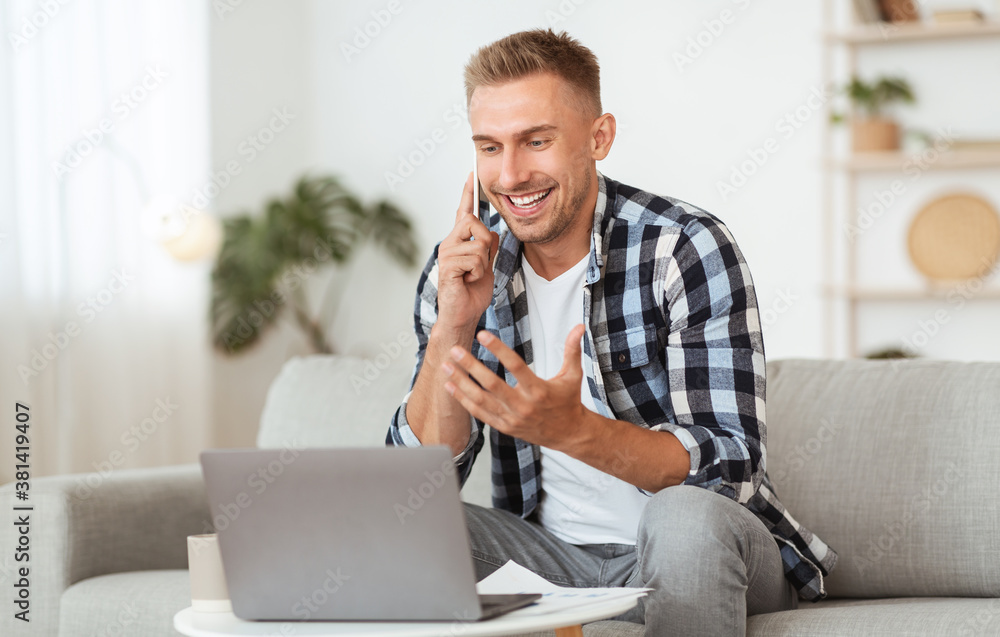 Wall mural Portrait of smiling guy using pc talking on phone