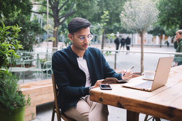 Young man writing in notebook while sitting in cafe