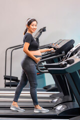 Fototapeta na wymiar Asian pregnant woman exercising in the gym on treadmill. Fitness and healthy lifestyle during pregnancy and smiling.