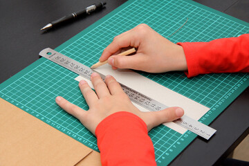 Hands draw a pencil on a ruler on a white sheet