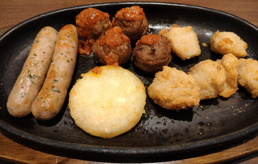 different fresh snacks on the black plate, like meat balls, fried chickens, sausages, potato pancake