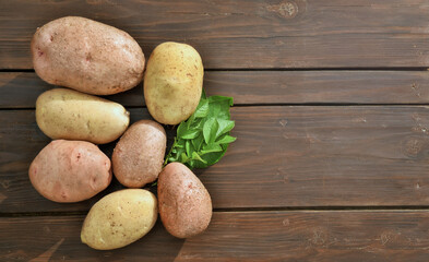 Fresh dug potatoes on a wooden table and against a background of green leaves.
