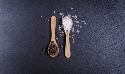 Salt and pepper in wooden spoon, top view