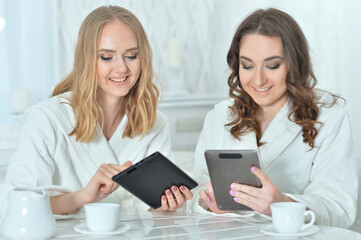 Young women in bathrobes using digital devices