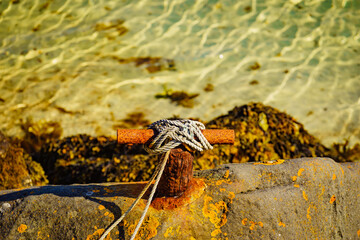 Old rusty mooring bollard with rope.