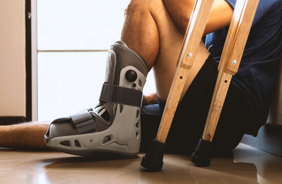 injured man broken ankle wearing ankle support sitting in the house with soft-focus and over light in the background