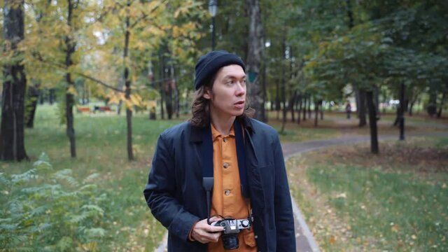 A Young Handsome Man with photo camera Walking along the Forest path in autumn day. Traveling Concept People in Nature. Hiker Journey in Wildlife