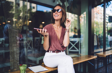 Smiling adult female browsing smartphone near cafe