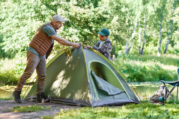 Full length portrait of father and son setting up tent together while enjoying camping in forest, copy space