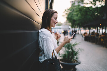 Smiling adult woman chatting on smartphone on street