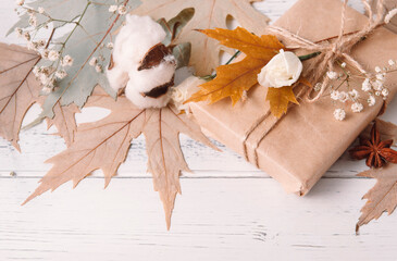 gift , dry maple leaves, white flowers on a white wooden background, autumn
