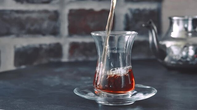 Red tea is poured from a copper metal teapot into a glass armudu glass. Close-up. Traditional Turkish Tea Party