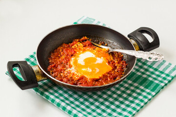 Eggs with tomatoes cooked in a pan with a handle on fabric napkin