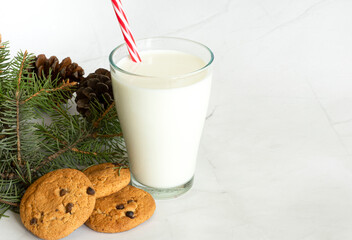 Milk in a glass with a straw, next to oatmeal cookies, close-up. Christmas drinks. Christmas tree. White marble background. View from above. Selective focus. Copy space. Banner