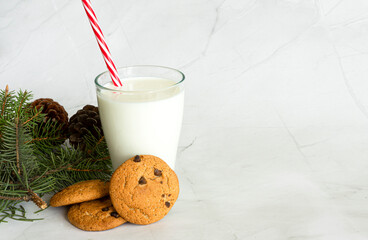 Milk in a glass with a straw, next to oatmeal cookies, close-up. Christmas drinks. Christmas tree. White marble background. Selective focus. Copy space. Banner