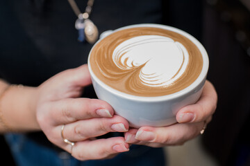 Barista girl holding fragrant freshly made cappuccino in her hands