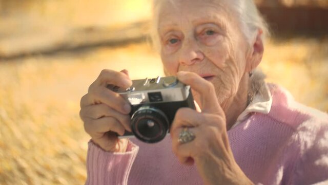 92 year old senior woman holding retro film camera outdoor on a sunny autumn day. Closup, shallow DOF.