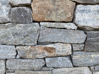 Detail of oddly shaped, grey and other earth-tone bricks in a wall made of rock, creating abstract background texture suitable for compositing