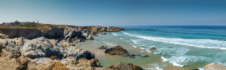 Wide panoramic image of beach with rocks and blue sea in background, natural landscape