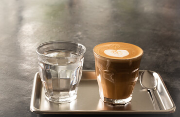 coffee latte in glass and water in glass on stainless steel tray on dark concrete table, minimal style coffee place.