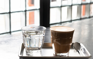 coffee latte in glass and water in glass on stainless steel tray on dark concrete table, minimal style coffee place.