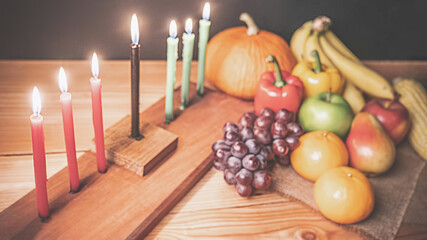 Obraz na płótnie Canvas Kwanzaa holiday concept with decorate seven candles red, black and green, gift box, pumpkin,corn and fruit on wooden desk and black background.