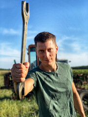Young smiling handsome worker with wrench outdoor near tractor