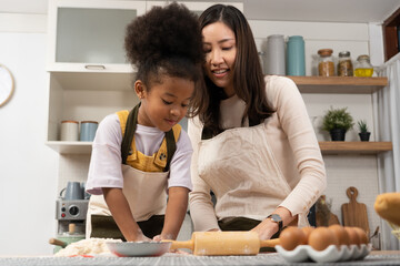 Fototapeta premium Asian woman and African little girl have fun cooking in home kitchen.