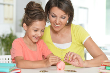 Portrait of mother and child daughter putting coins into piggy bank