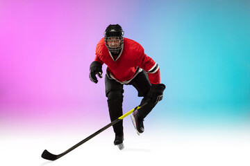 Winner. Male hockey player with the stick on ice court and neon gradient background. Sportsman wearing equipment, helmet practicing. Concept of sport, healthy lifestyle, motion, wellness, action.