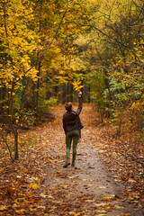 Young woman wearing brown leather jacket and green trousers walking in the autumn forest.